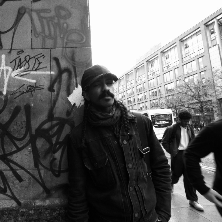Uzmaan standing beside a graffiti-covered wall on a city street